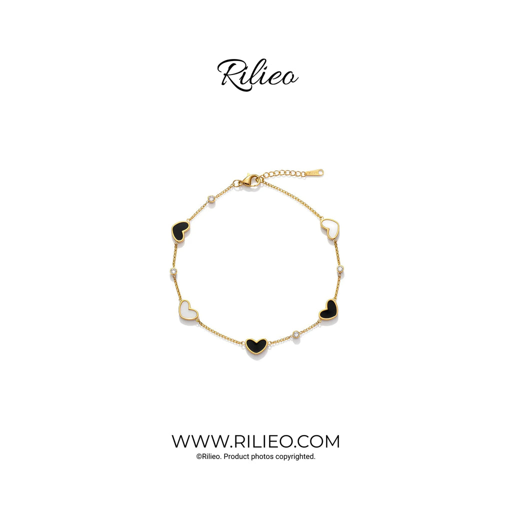 Gold plated heart charm bracelet with black and white enamel accents on white background