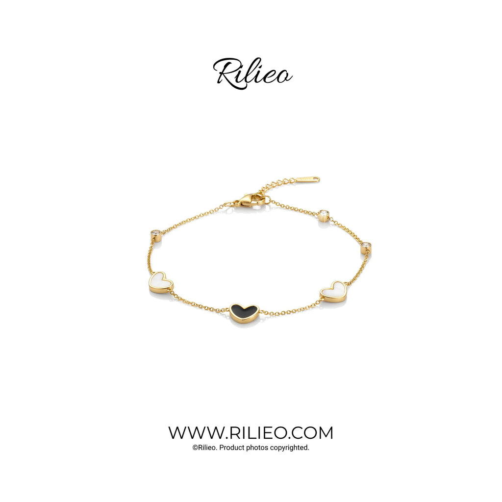Gold plated bracelet with black and white heart charms and adjustable chain on white background