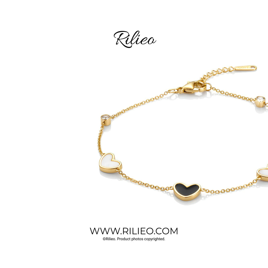 Gold plated heart charm bracelet with black and white enamel accents on a white background